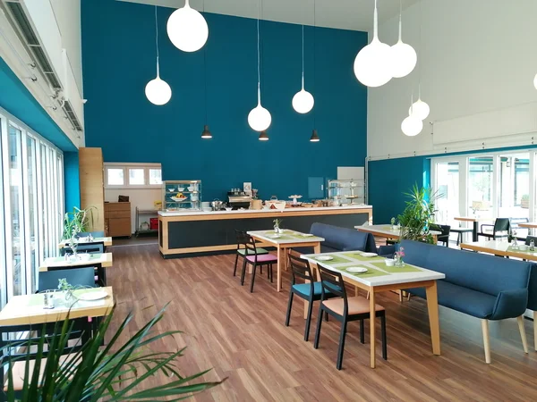 Modernes Café mit Holzboden, blauen Wänden, weißen Lampen und Pflanzen.