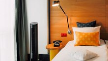 Teil des Hotelzimmers mit Bett, Wandlampe und bunten Kissen